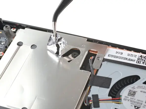 Retire la cinta de aluminio con unas pinzas para descubrir el tornillo oculto en el protector de la placa en el proceso de actualización de Steam Deck SSD.
