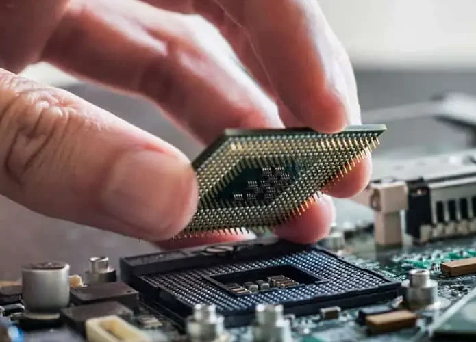 Picture of a hand holding a CPU (Central Processing Unit) extracted from a laptop, showcasing the delicate process of removing and replacing hardware components.