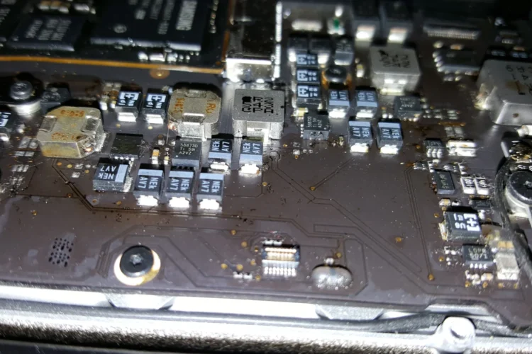 Componentes internos de una MacBook Pro que muestran daños por agua, con signos de corrosión y humedad en los circuitos y el hardware.