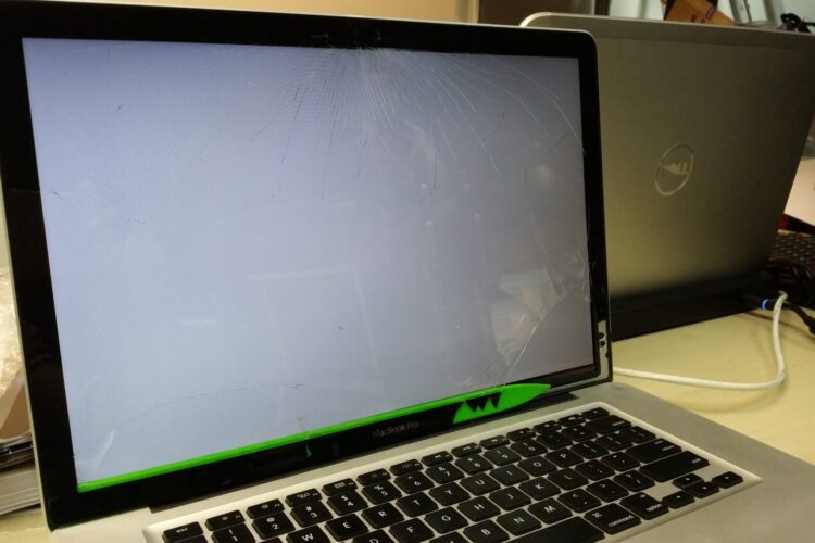 Una imagen de una MacBook con la pantalla rota, que muestra fragmentos de vidrio rotos y líneas irregulares en la superficie de la pantalla.
