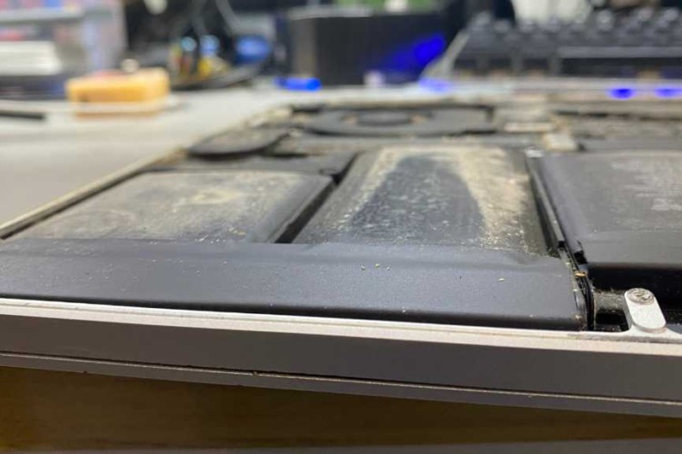 The photo depicts the internal view of a MacBook A1398 with a clearly visible bloated battery. The battery cells have expanded, causing deformation and pushing against the laptop's frame.