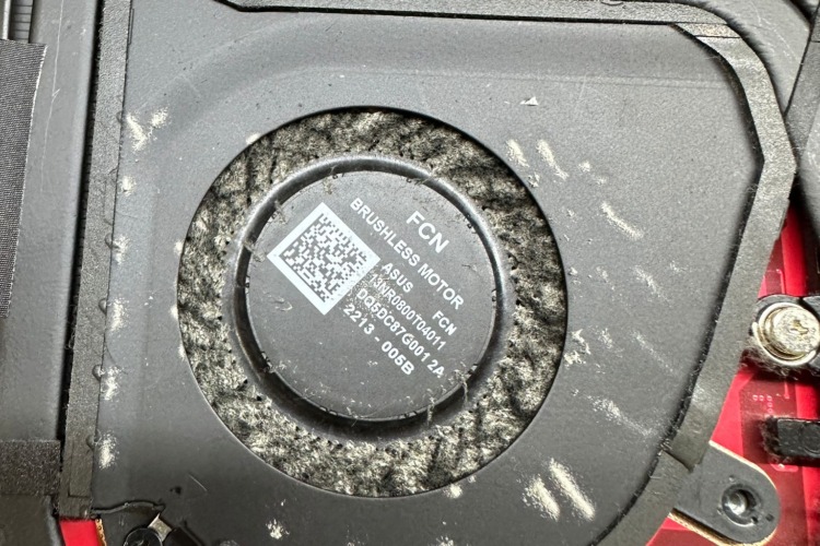 A close-up photograph of a laptop fan reveals a thick layer of dust and debris completely covering the blades and surrounding area. The dust buildup is significant, blocking airflow and hindering the fan's ability to cool the laptop. The image serves as a stark visual reminder of the importance of regular maintenance and cleaning to prevent laptop overheating.