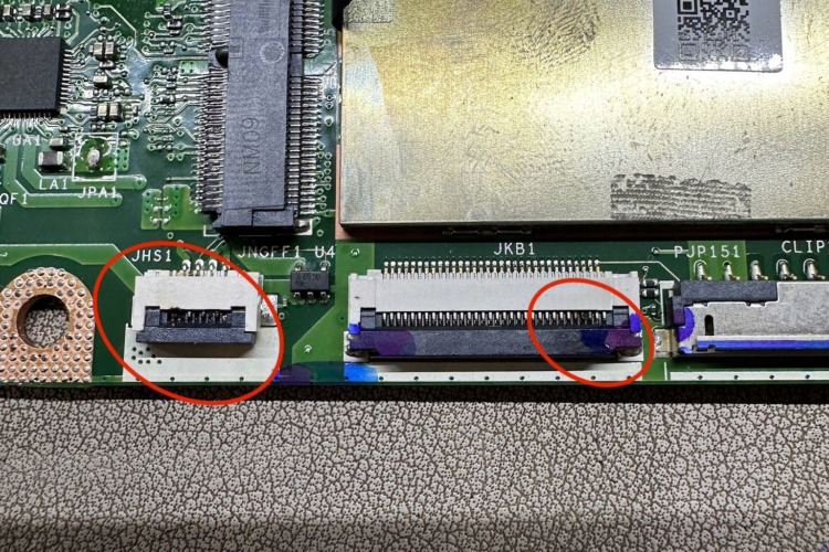 A circuit board with red circles highlighting a connector and board edge, suggesting areas of concern, possibly water damage, against a textured background.