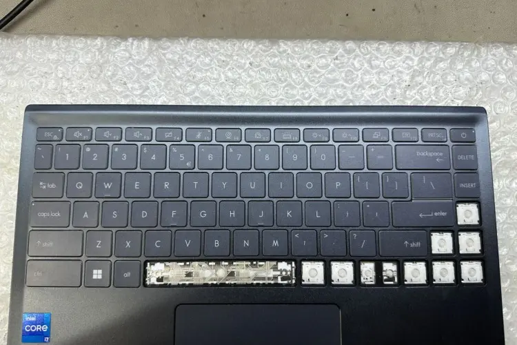 The image shows a laptop keyboard with several keys on the right side missing, exposing the underlying mechanism. The laptop appears to be on a desk with a bubble wrap sheet underneath it. 