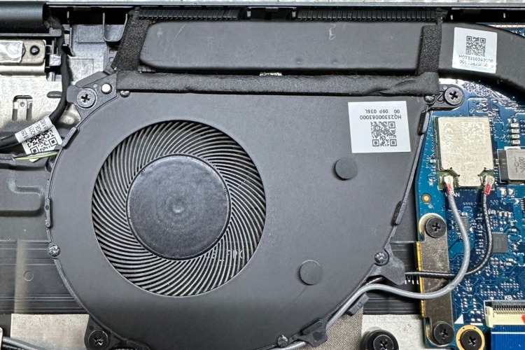 The image shows a clean laptop cooling fan after the removal of dust, situated within the open casing of the laptop. The fan blades and the vent area are now free of debris, showcasing the fan's details, including the manufacturer's label with identification numbers.