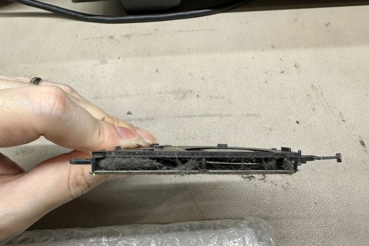 a hand holding a very dusty laptop heat sink, indicating that it has been removed from the laptop. The heat sink fins are clogged with dust, which can impede the laptop's cooling efficiency. 