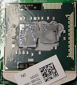 A close-up photograph reveals the top of a laptop's CPU with dried-out thermal paste applied. The once-silvery paste has cracked and discolored, losing its smooth consistency and becoming hard and brittle. The dried-out paste is no longer effective in transferring heat away from the CPU, potentially causing overheating issues. The image serves as a visual indicator of the need for thermal paste replacement to maintain optimal laptop performance.