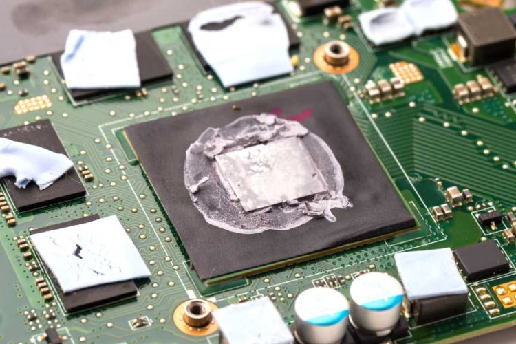  This image shows a close-up of a laptop's internal circuit board with a focus on the central processing unit (CPU). The CPU has a gray, patchy substance on its surface, which appears to be old or improperly applied thermal paste that may need cleaning or replacement.
